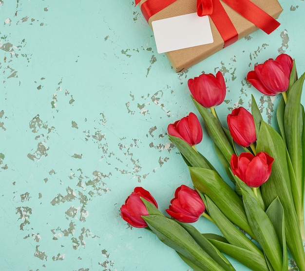 Bouquet of red blooming tulips with green leaves, wrapped gift in brown craft paper and tied with a silk red ribbon