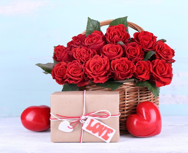 Bouquet of red roses in basket with present box on wooden background