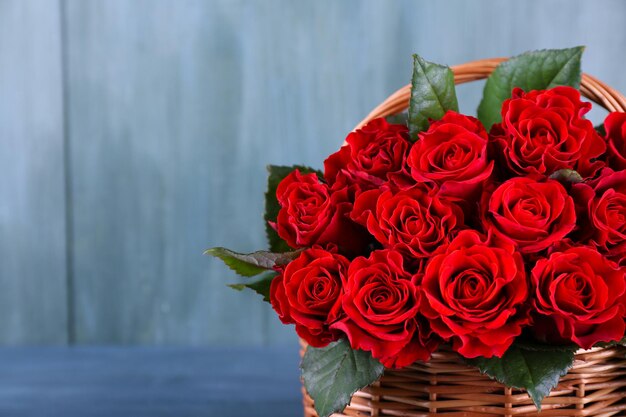 Bouquet of red roses in basket on wooden background