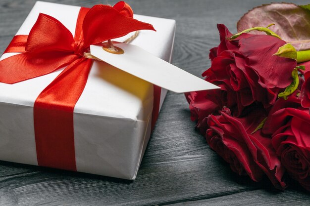 A bouquet of red roses, gift and hearts on table