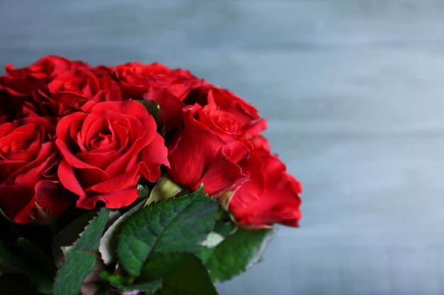 Bouquet of red roses in glass vase on wooden background