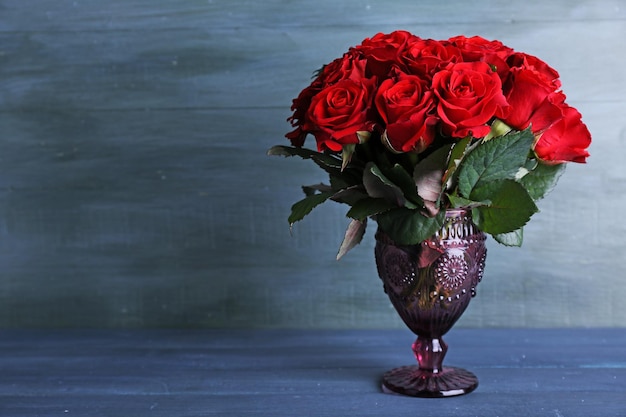 Букет красных роз в стеклянной вазе на деревянном фоне