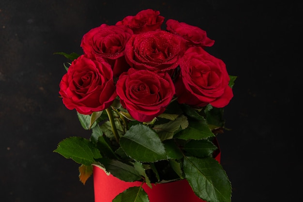 Bouquet of red roses in red pot on dark background.