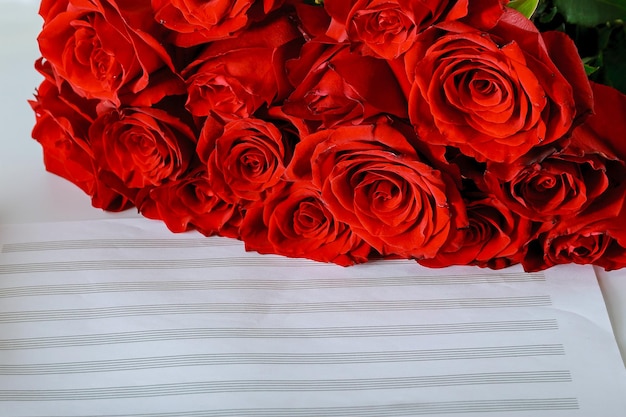 Foto bouquet di rose rosse su un foglio per lo spazio della copia delle note musicali