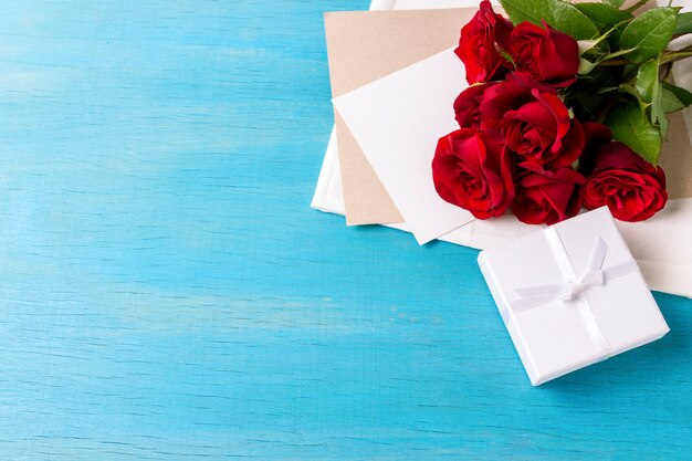 Bouquet of red roses White gift box clean sheet, blue wood background. Copy space. Romantic gift for Valentine's Day holiday