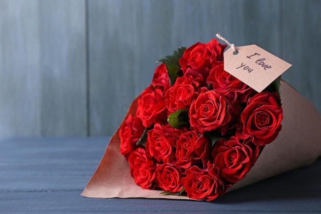 Bouquet of red roses with tag wrapped in paper on wooden background