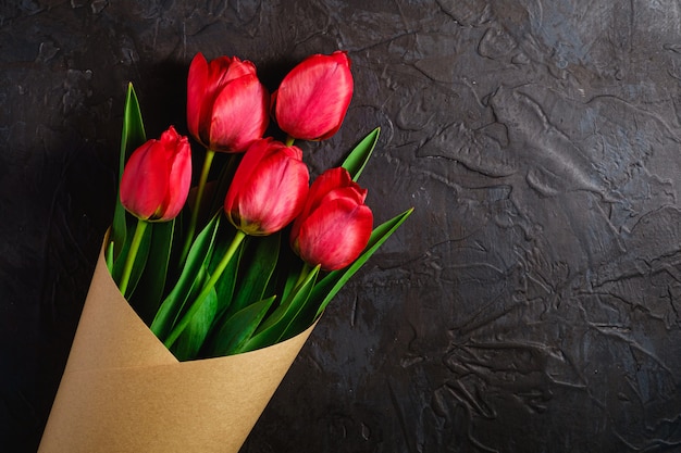 Bouquet of red tulip flowers on textured black background, top view copy space