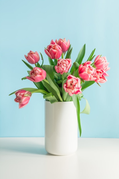 Bouquet of red tulip in vase on blue. 