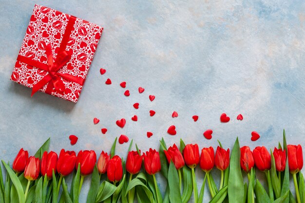 Bouquet  of red tulips, gift box with red ribbon and red heart figurines.