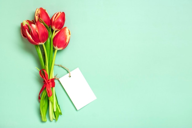 Bouquet of red tulips notepad on green background Top view Flat lay