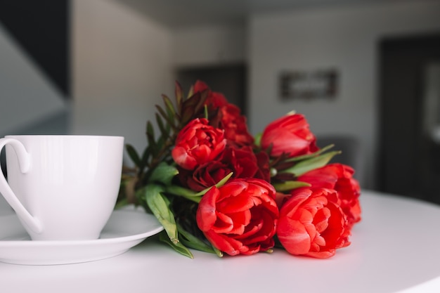 A bouquet of red tulips on the table and a white cup of coffee. Concept for a greeting card. 