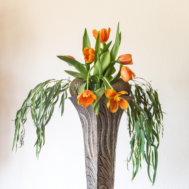 A bouquet of red tulips in a tall art business vase on a table with a yellow tablecloth.