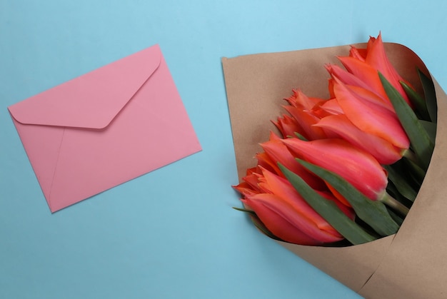 Bouquet of red tulips with an envelope on a blue