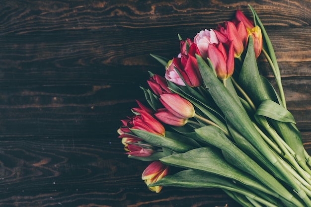 Bouquet of red tulips on a wooden table in a dark style