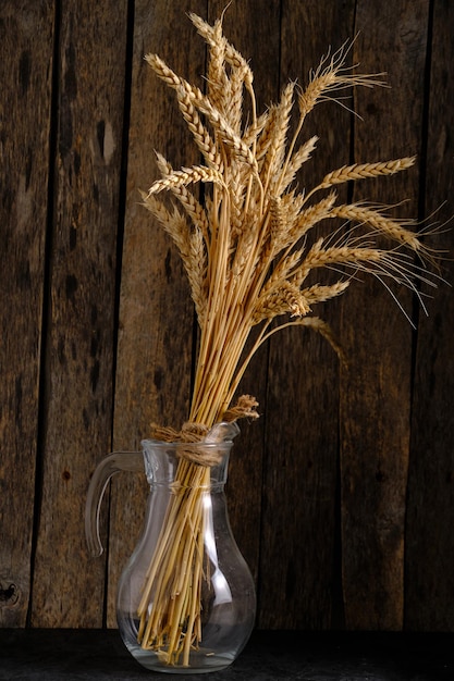 Bouquet ripe wheat ears in glass jug wooden background