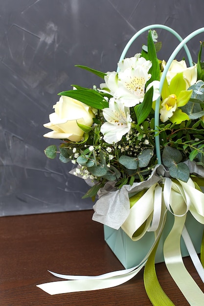 Bouquet of roses astralmeria and lilies in a basket of light green color on a gray background