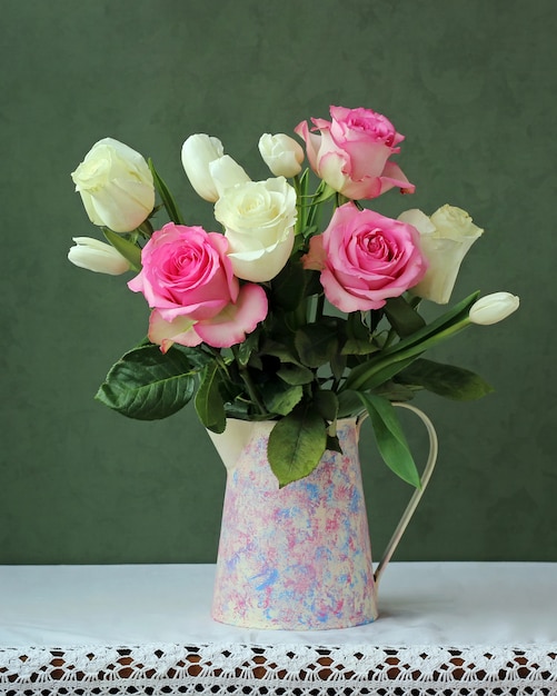 A bouquet of roses and tulips in a jug on table 