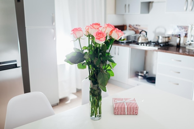 女性のバレンタインデーのモダンなキットのキッチンサプライズにカードとギフトボックスを残したバラの花束