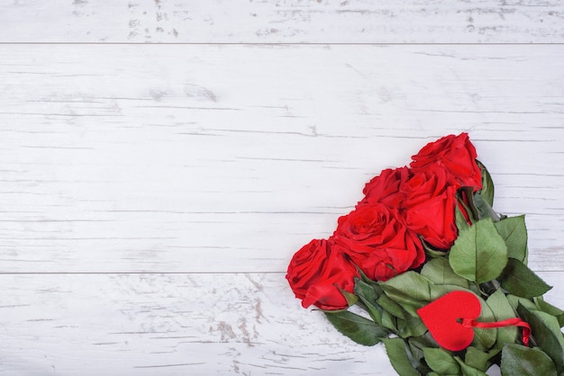 Bouquet di rose con cuore decorativo e nastro su fondo di legno bianco.