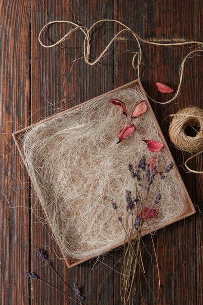 A bouquet of several dried lavender branches, dry petals and a thread on a deoeval tray on an old wooden table flat lay
