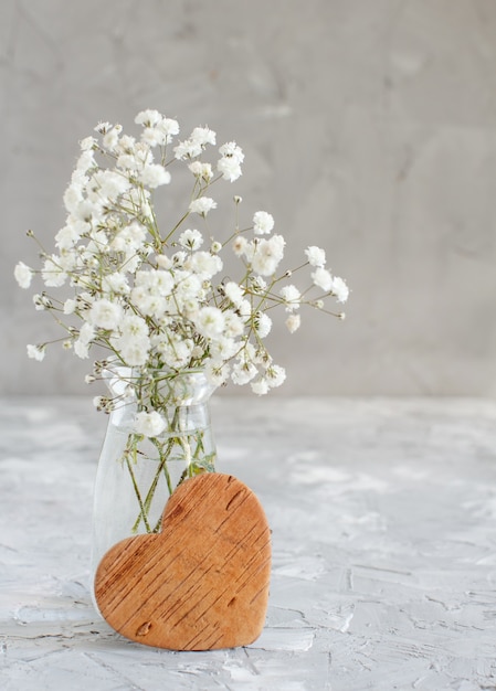 Bouquet of small white flowers and wooden hearts on a grey background