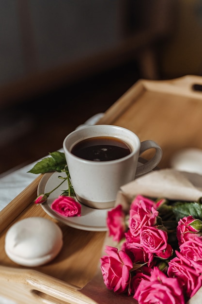 Bouquet of spring flowers and a cup of coffee on a wooden tray in bed