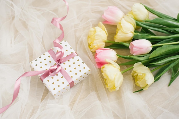 A bouquet of spring tulip flowers and a gift box with a pink bow on a beige fabric background for mother's day Flat lay
