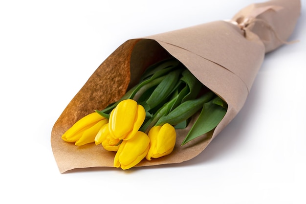 Букет весенних тюльпанов с желтыми цветами, завернутый в крафт-бумагу для подарка на белом фоне