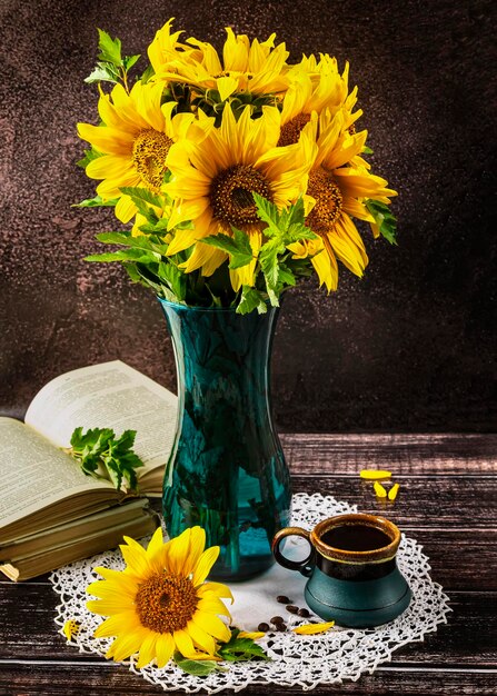 A bouquet of sunflowers in a blue vase on a dark background a blue cup and an open book