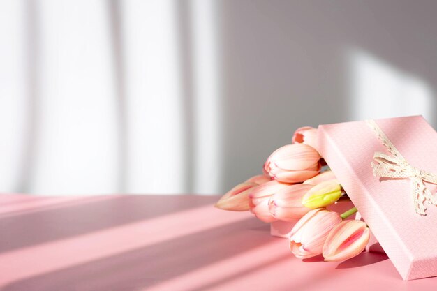 Bouquet of tender tulips and gift box isolated on pink background with shadow. Spring flowers. Greeting card for Birthday, Woman, Mother's Day, Wedding, Valentine's day. Copy space