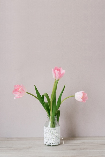 Bouquet of three pink tulips stands in a glass vase with lace. 
