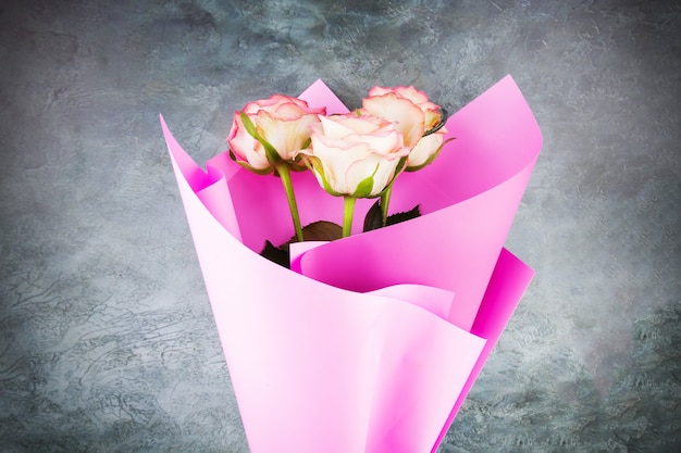 Bouquet of three roses in a pink wrapper on gray background