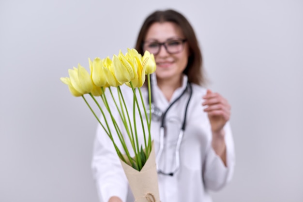 聴診器を持つ女性医師の手にチューリップの花の花束。世界保健デー、灰色の背景に花と幸せな看護師