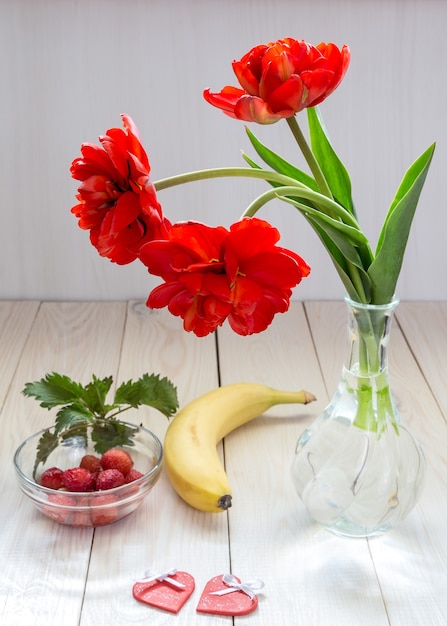 Bouquet of tulips, banana and strawberries on a wooden table.