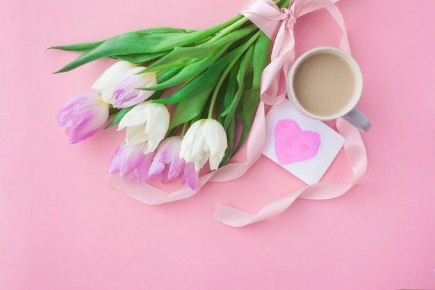 Bouquet of tulips and a coffee cup on a pink pastel background