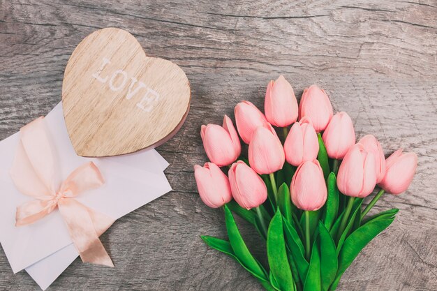 Bouquet of tulips and an envelope on a wooden background, top view.