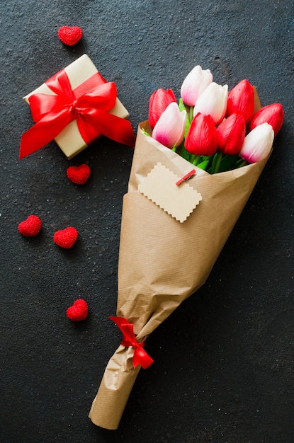 Bouquet of tulips and gift box on dark background.