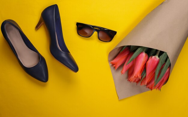 Bouquet of tulips, high-heeled shoes with sunglasses on a yellow