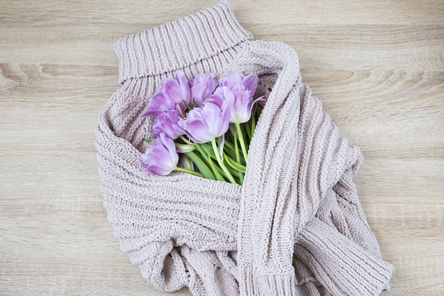 A bouquet of tulips is wrapped in a coarse knit woolen sweater