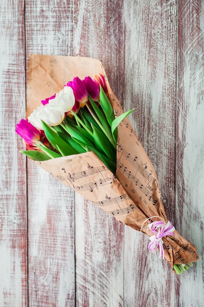 The bouquet of tulips is wrapped in a paper isolated on wood