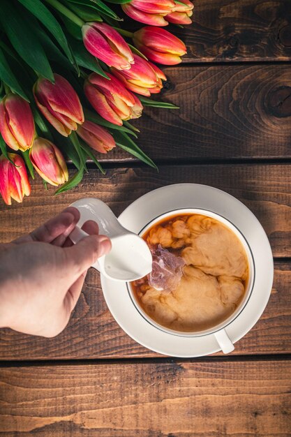 A bouquet of tulips lies on a wooden table next to a coffee\
mug