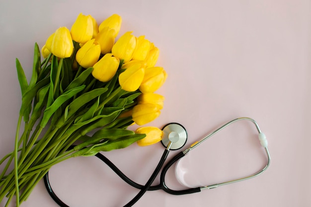 A bouquet of tulips and a stethoscope on a pink background. Top view with copy space. National Doctor's Day. Happy Nurse's Day.