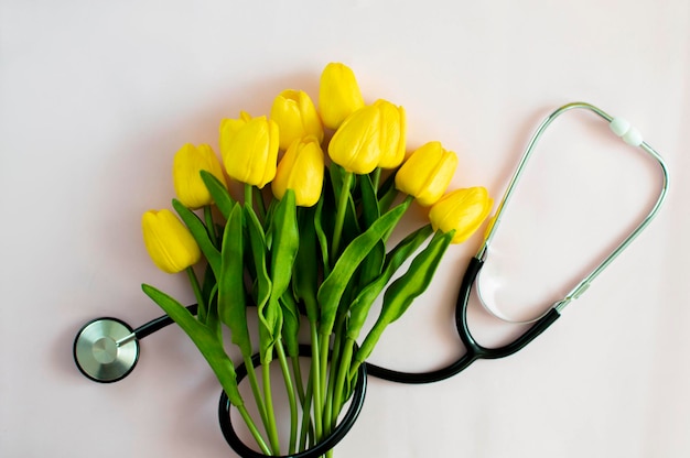 A bouquet of tulips and a stethoscope on a pink background. Top view with copy space. National Doctor's Day. Happy Nurse's Day.