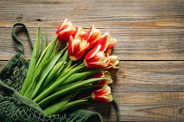 木製の背景のストリングバッグの中のチューリップの花束 ⁇ 母の日 ⁇ 女性の日 ⁇ のトップビューコンセプト