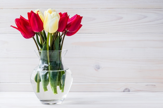 Bouquet of tulips in vase on wooden background. Empty place for text.