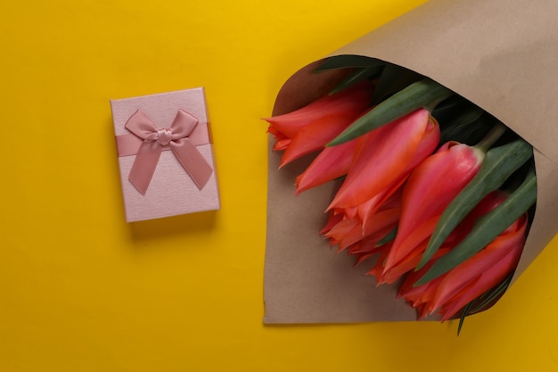 Bouquet of tulips with gift box on a yellow