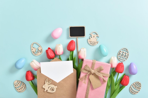 A bouquet of tulips with a postcard a gift and wooden Easter eggs with a plaque on a light blue background