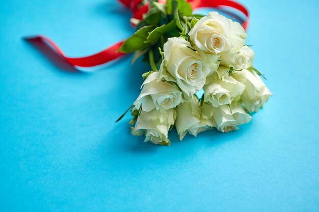 Bouquet van witte rozen met rode strik op blauwe achtergrond Valentijnsdag of liefdesconcept afbeelding Bloemelijke achtergrond afbeelding met kopieerruimte voor tekst