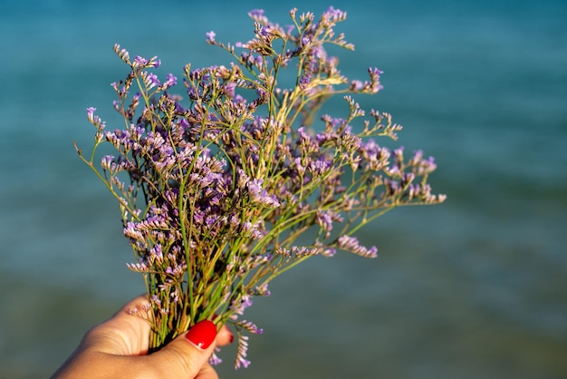 Bouquet of violet flowers in woman hand on the sea background Hand holding lavender