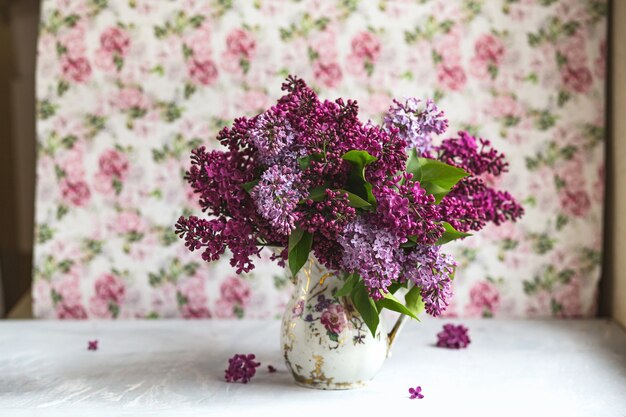 Bouquet of violet lilac in a vintage shabby vase. Still life with blooming branches of lilac in vases. Free style photo.